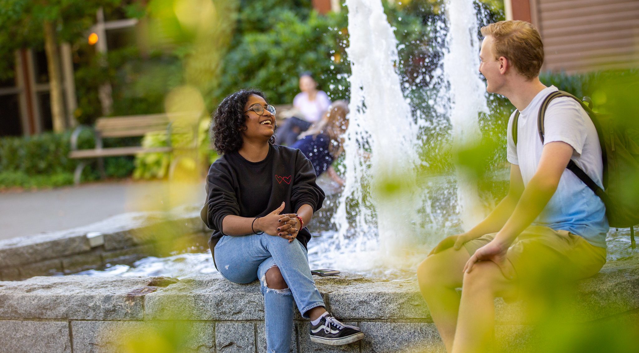 Two students sitting in front of a water fountain talking animatedly.